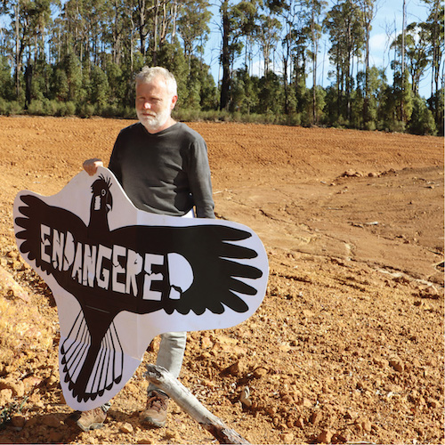 Man with  a sign like a black cockatoo in a cleared minesite
